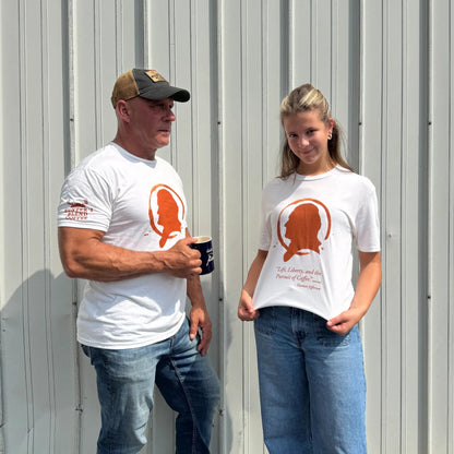 A man and a woman standing outdoors in front of a corrugated metal wall, both wearing matching white graphic T-shirts with an orange silhouette design and red text.